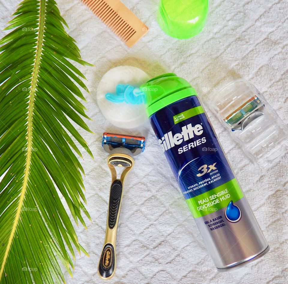 Gillette shaving cream and razor on a white towel with comb and palm leaf.