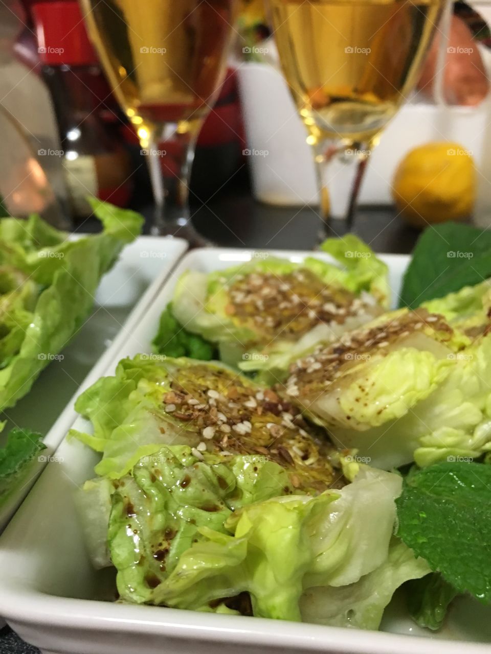 Baby berg lettuce salad with balsamic dressing topped with dukkah, closeup wine glasses in background, 