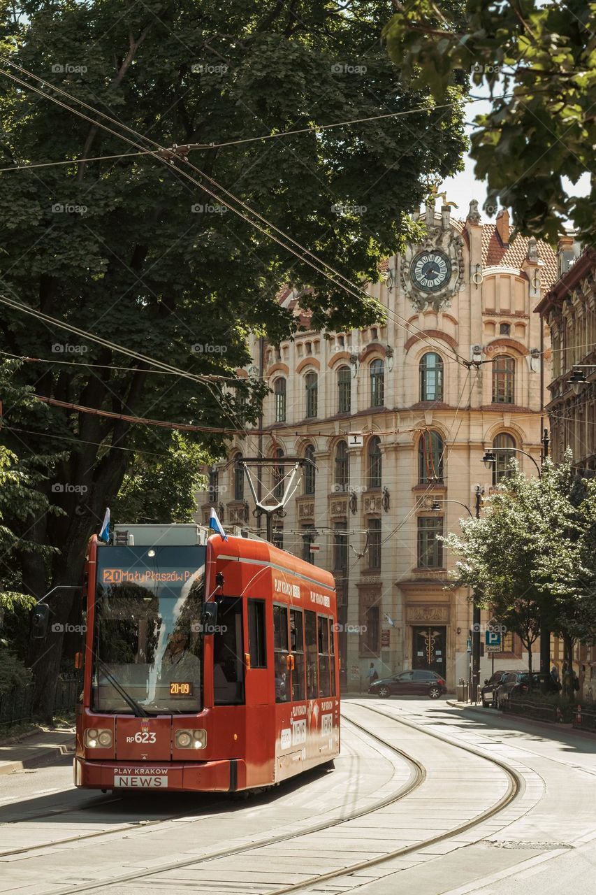 the tram goes along the street along the Planty park in Krakow in the background a beautiful school building