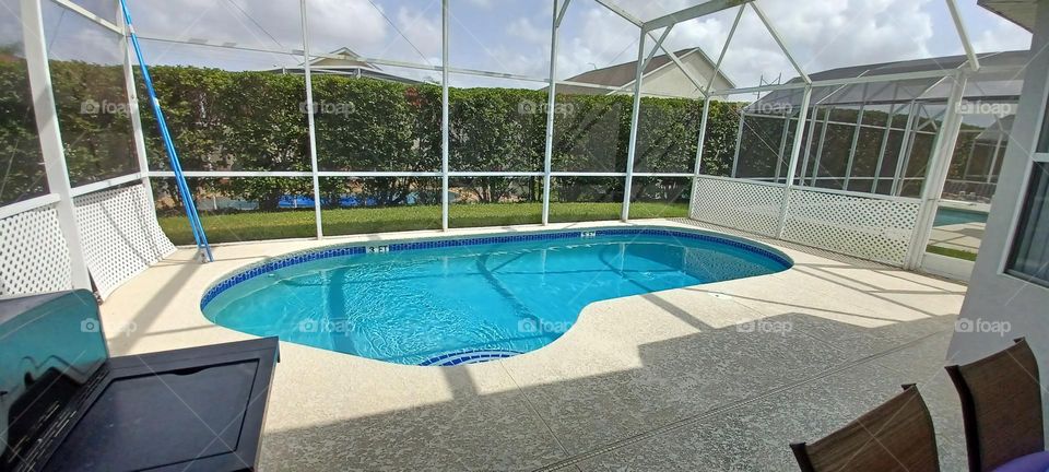 Frame of a screened in outdoor pool area and patio for outside entertainment with a brilliant shade of blue that makes the area pop 