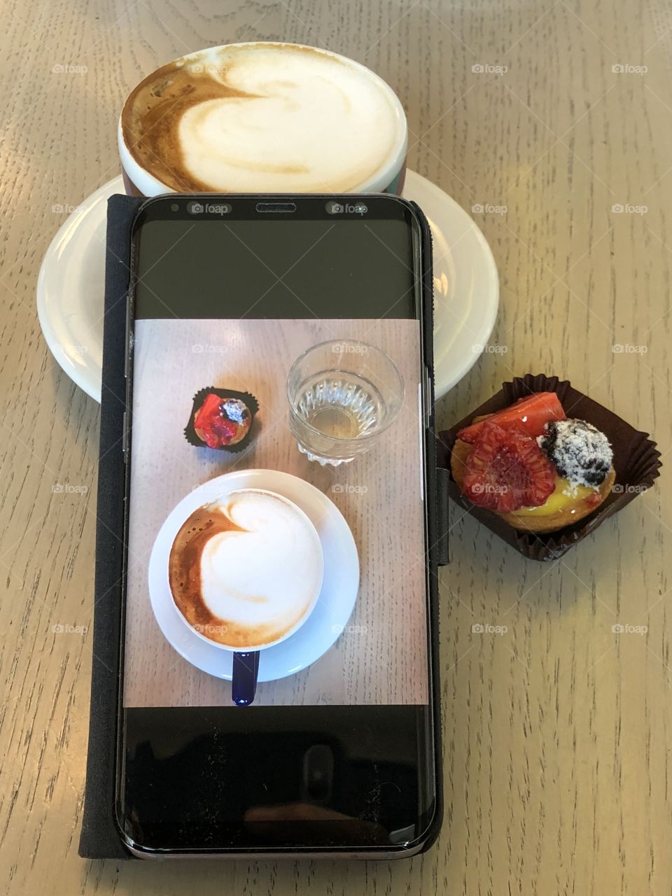 Breakfast with cappuccino, fruits pastry and a smartphone at the bar 