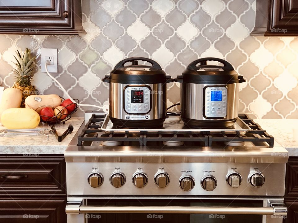 Two Instant pots sitting on top of a cookie sheet on top of a stove. 