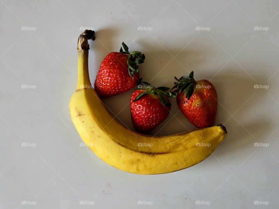 A banana and some strawberries placed on a table with a white background.