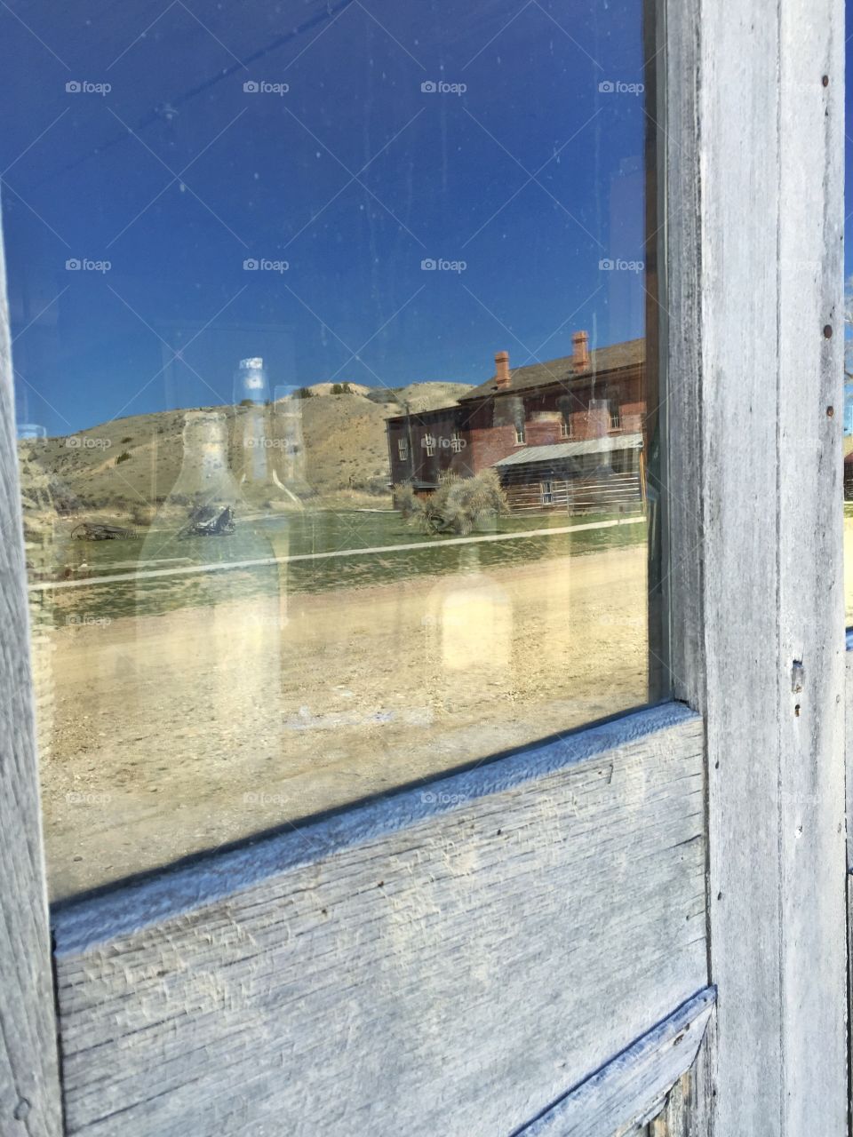 Ghost town reflected on an old window. Old bottles visible through window.  