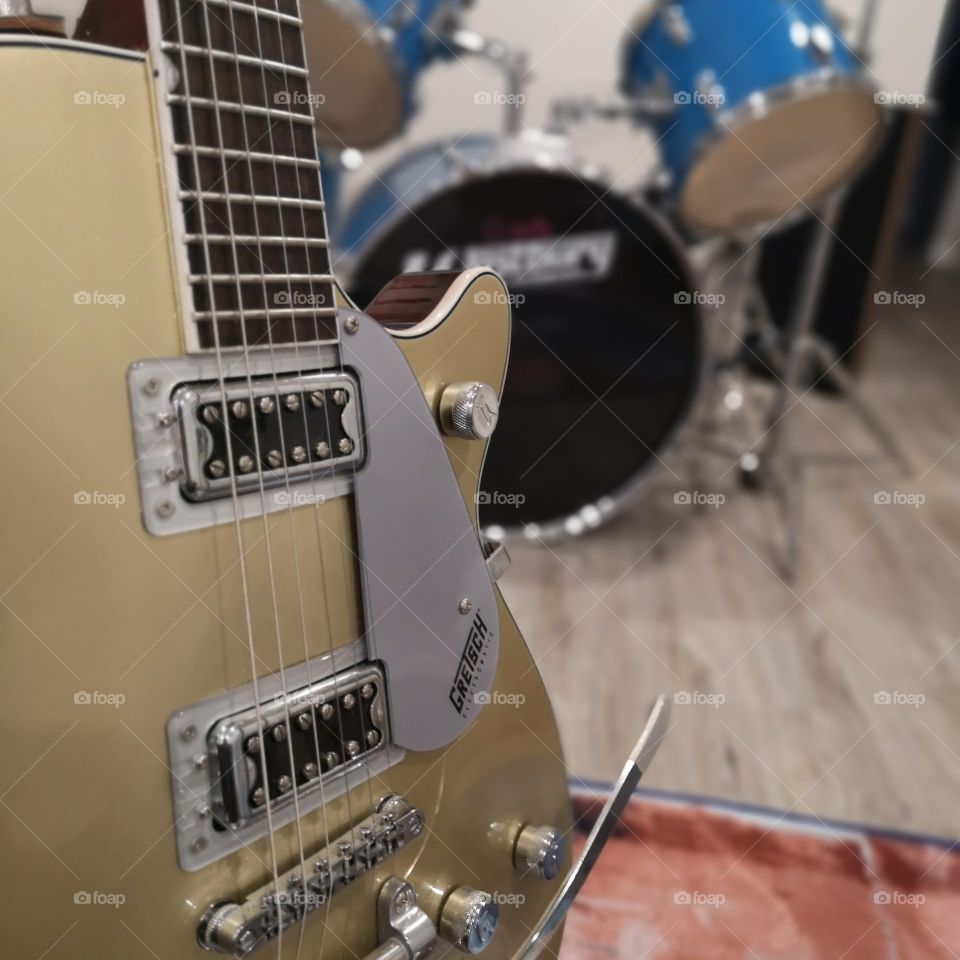 a gold guitar in front of some blue drums
