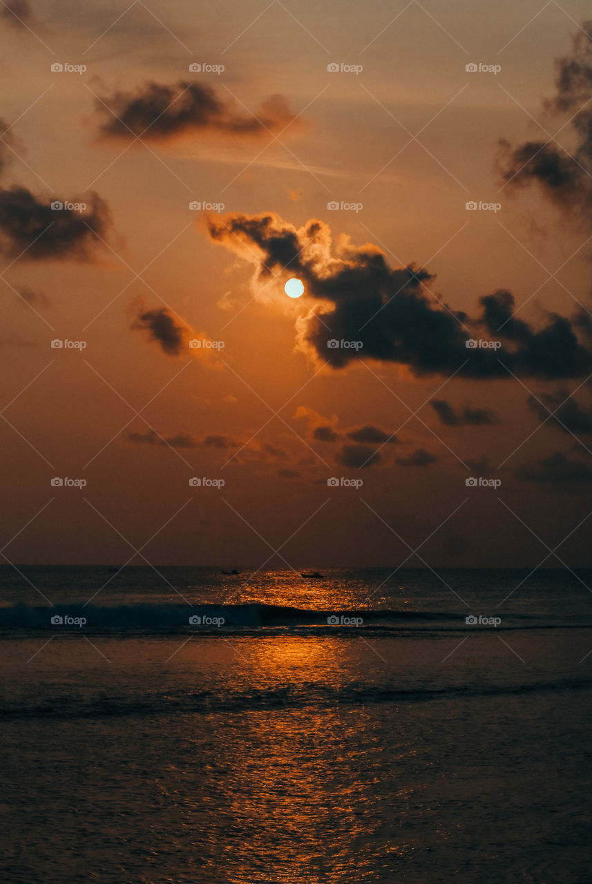 the moment when the sun goes down with a view of the beach and the waves are calming and there are 3 fishing boats far away