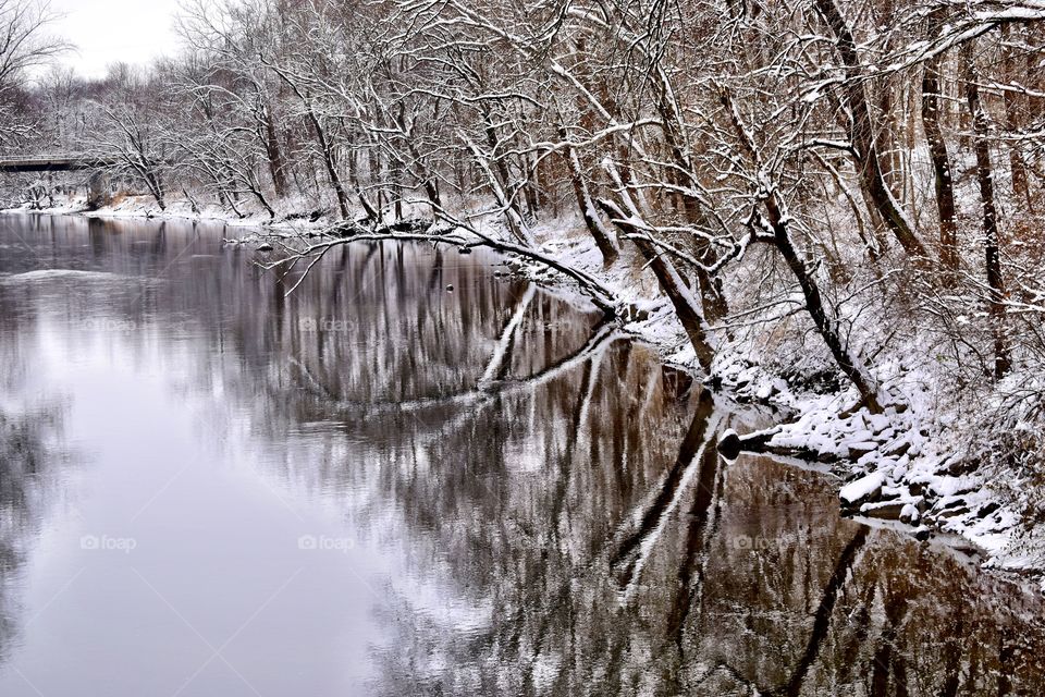 Snow on the river on a winter day with the trees reflecting off the water in Indiana 