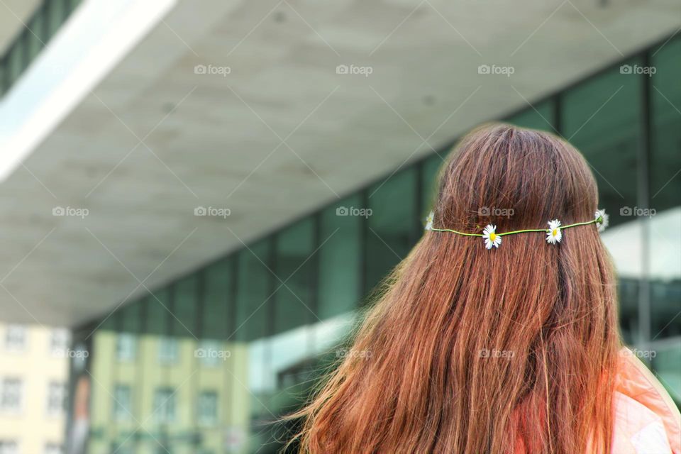 Rear view of a red-haired young woman with a flower wreath of daisies in her hair in the city