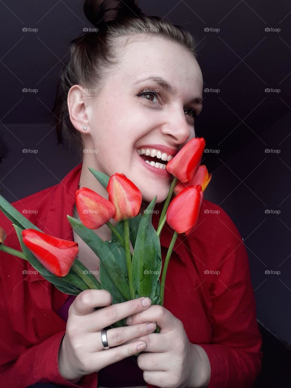 portrait of a light-skinned girl holding a bouquet of bright red tulips near her face and smiling