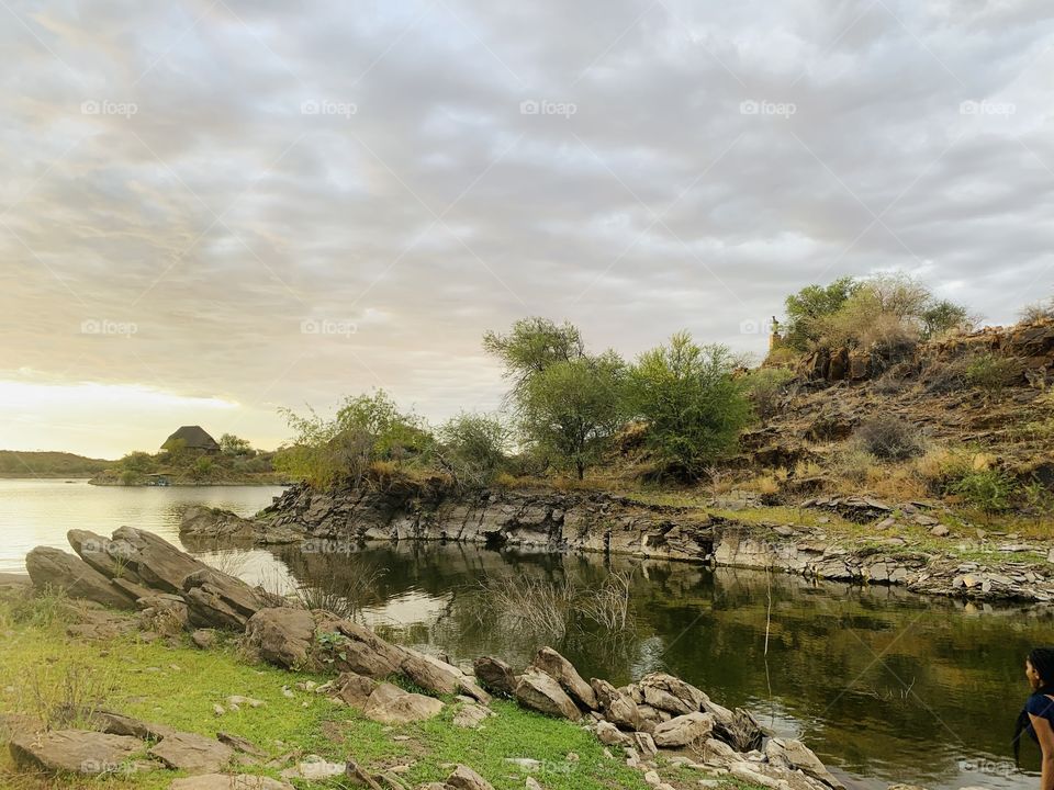 Picture of a lake full of water with a soft mute cloudy background. Natural views of water, plants, air, rocks. 