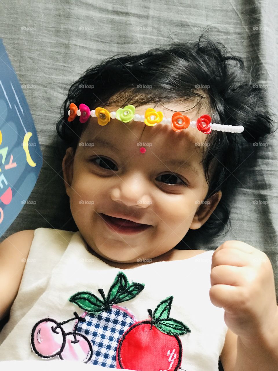 Indian baby girl with cute smile and wearing multi colour hairband 