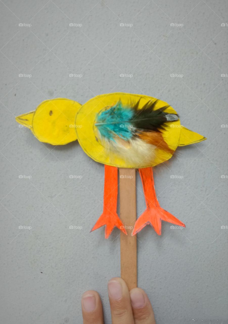 A chick made from reusable box paper, crayon, ice cream stick and some pieces of feather duster.