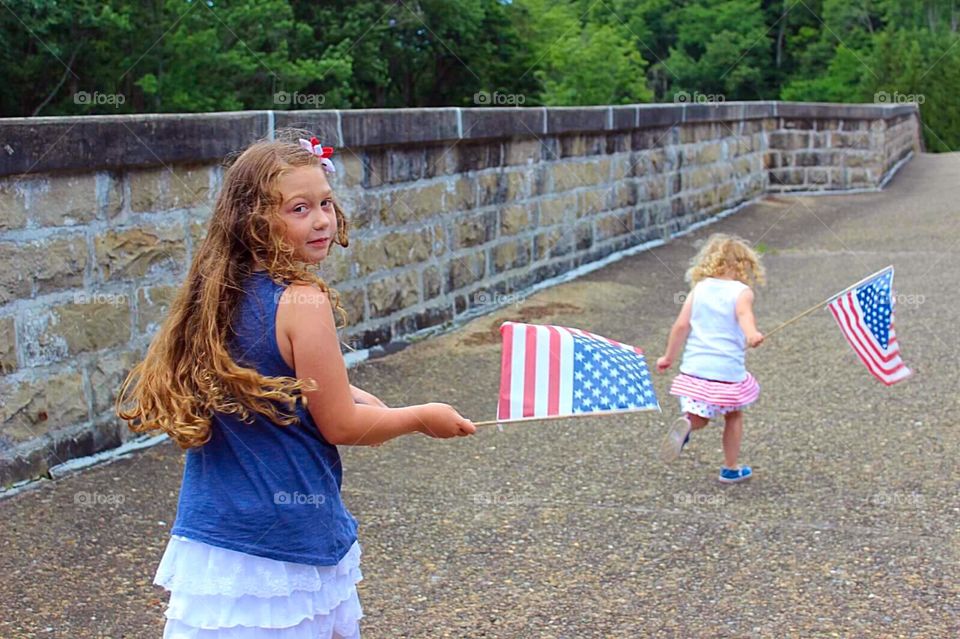 Two adorable little sisters holding American flags
