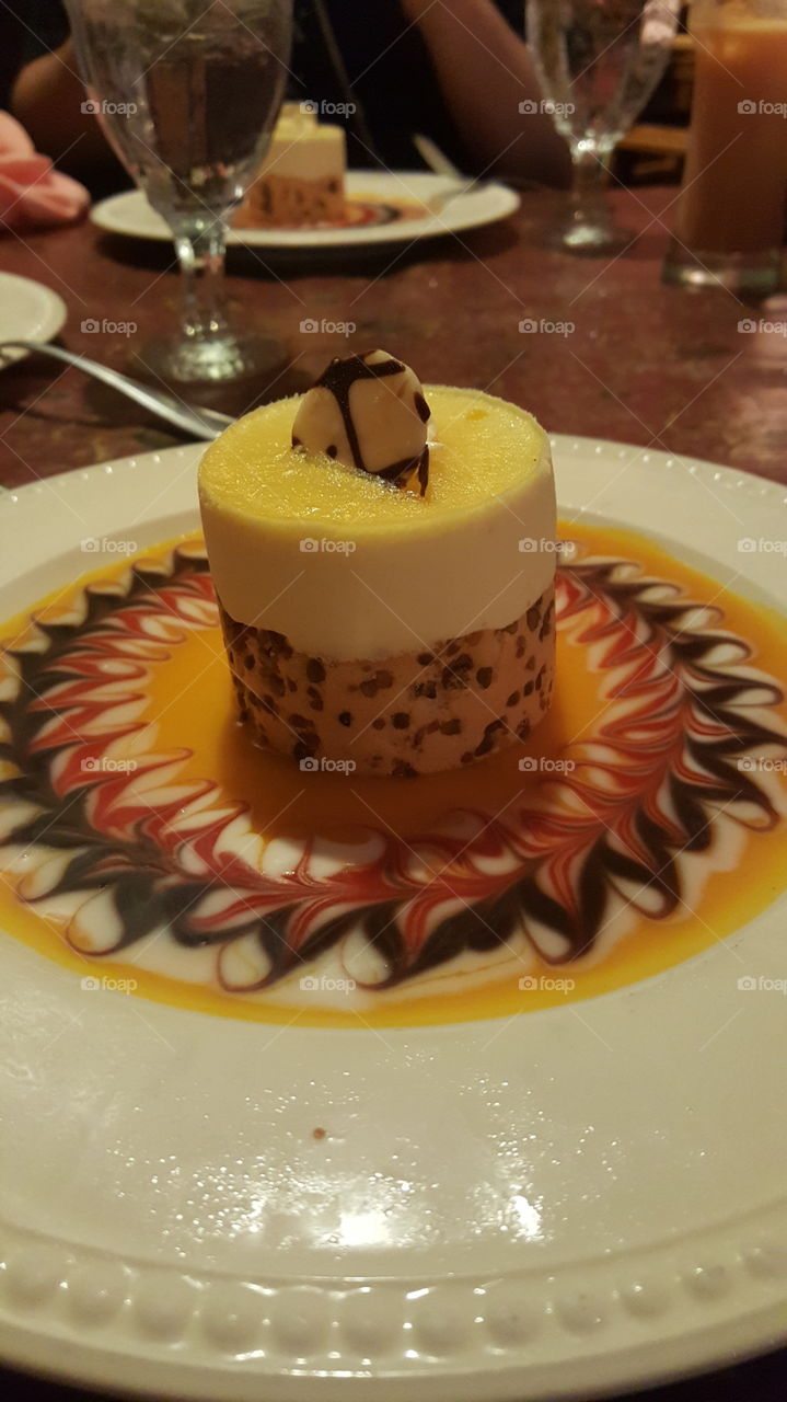 A light dessert. A mango mousse and pistachio cake treat, decorated with syrups.