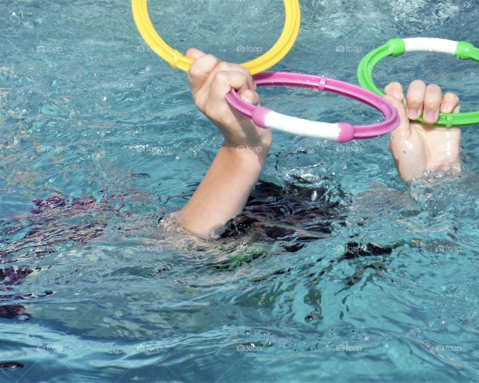 Summertime fun. Boy underwater holding colorful diving rings above the water