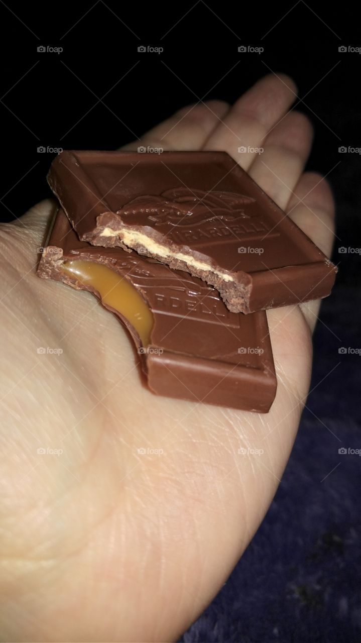 a bite taken out of two Ghirardelli milk chocolate squares one filled with almond and the other caramel