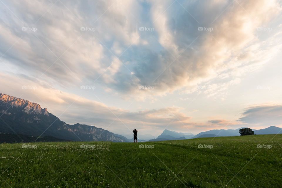One man on the top of a green hill under beautiful clouds at sunset in the mountains of Kufstein Austria 