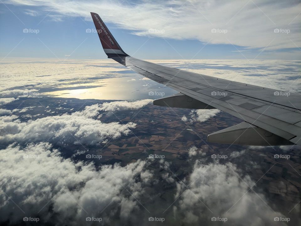 Flying through the air. The wing of the airplane over wispy clouds and the land below.