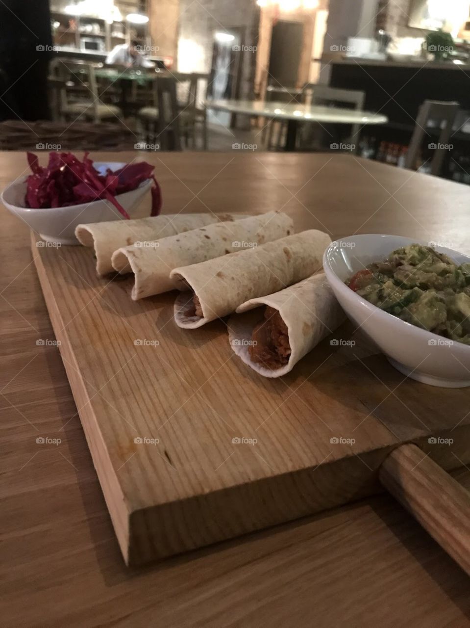 Tacos on a wooden board with guacamole and pickled onions in a restaurant 