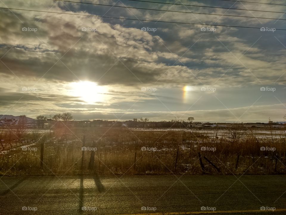 sun through clouds with shy rainbow peeking over Farm field