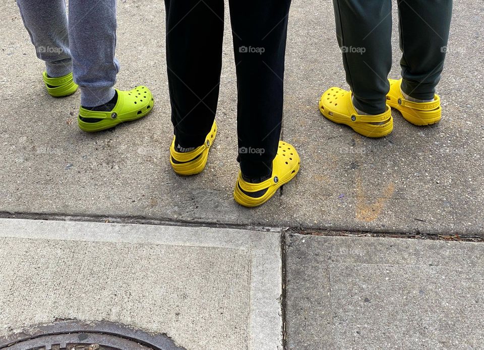 Three people wearing similar brightly colored Crocs standing on a sidewalk 