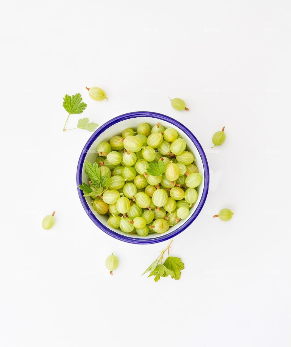 A bowl of green gooseberries on a white background.