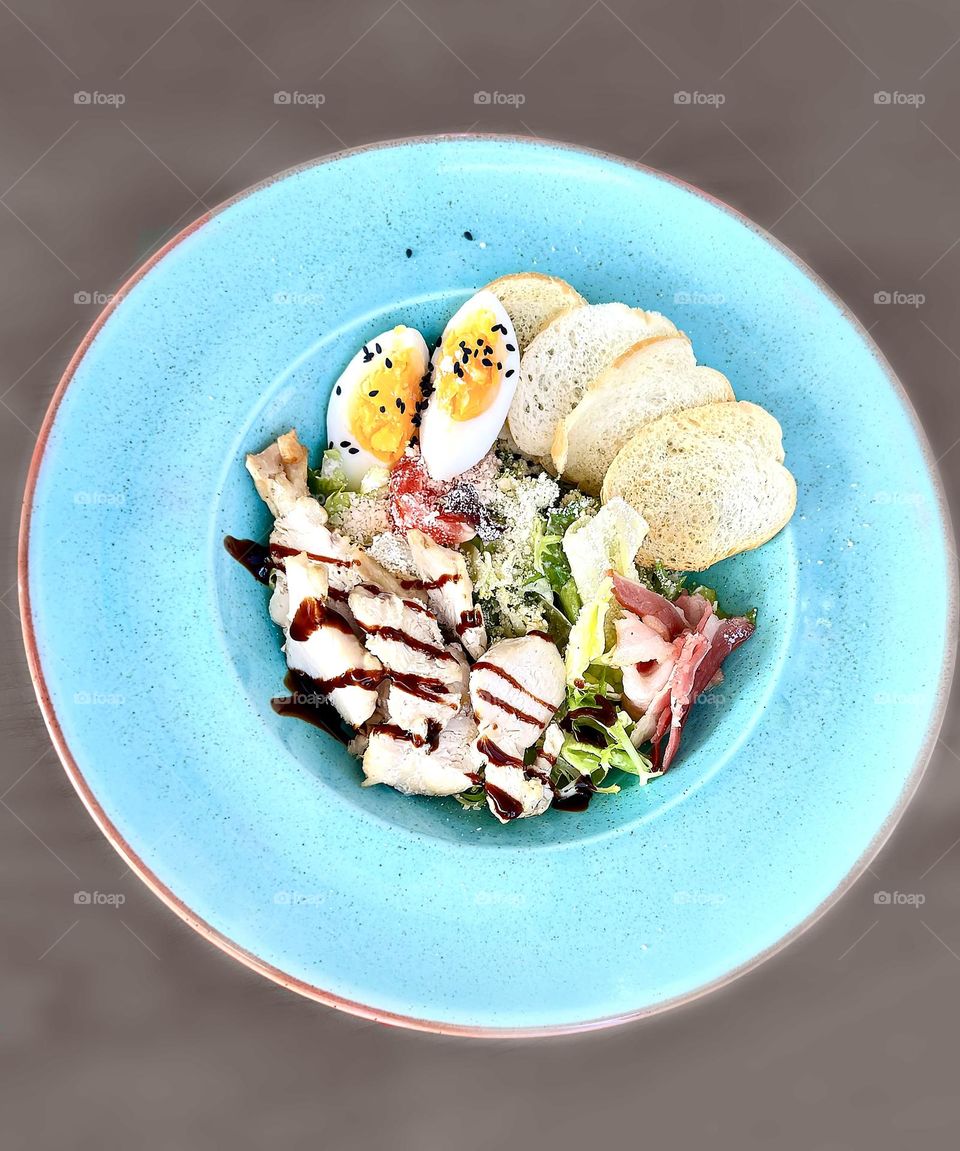 Salad with chicken breast, bacon, egg, herbs sprinkled with cheese in a large blue plate