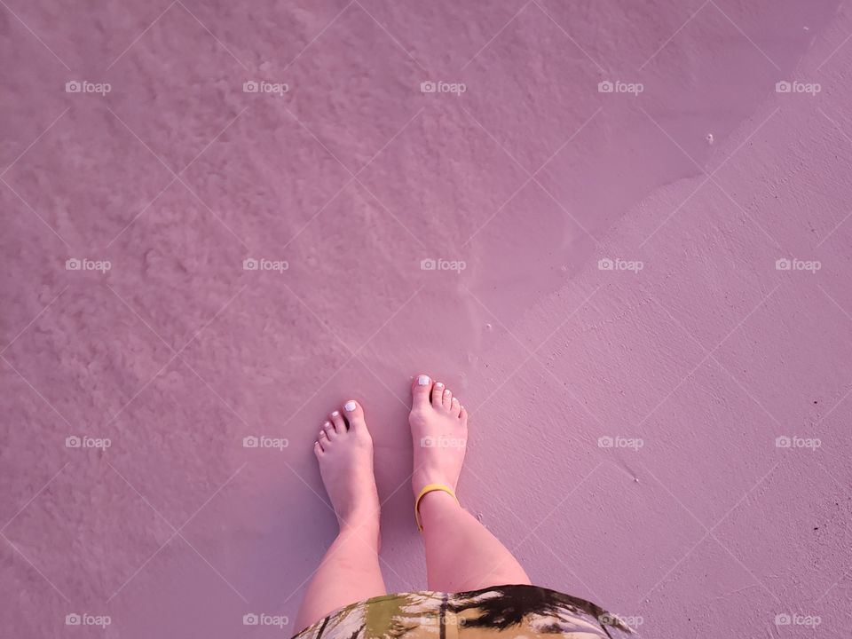 View from above, looking down at feet in sand with ocean tide pulling away. Sunset pink glow on feet and sand, on vacation in Mexico.