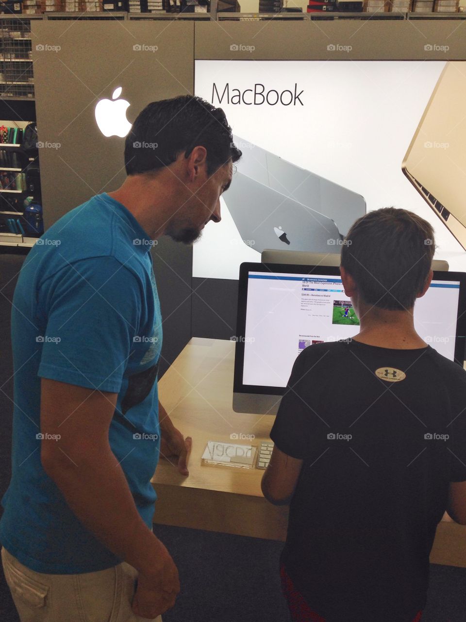 To Apple or not to Apple . Man and boy trying out a large screen Mac book