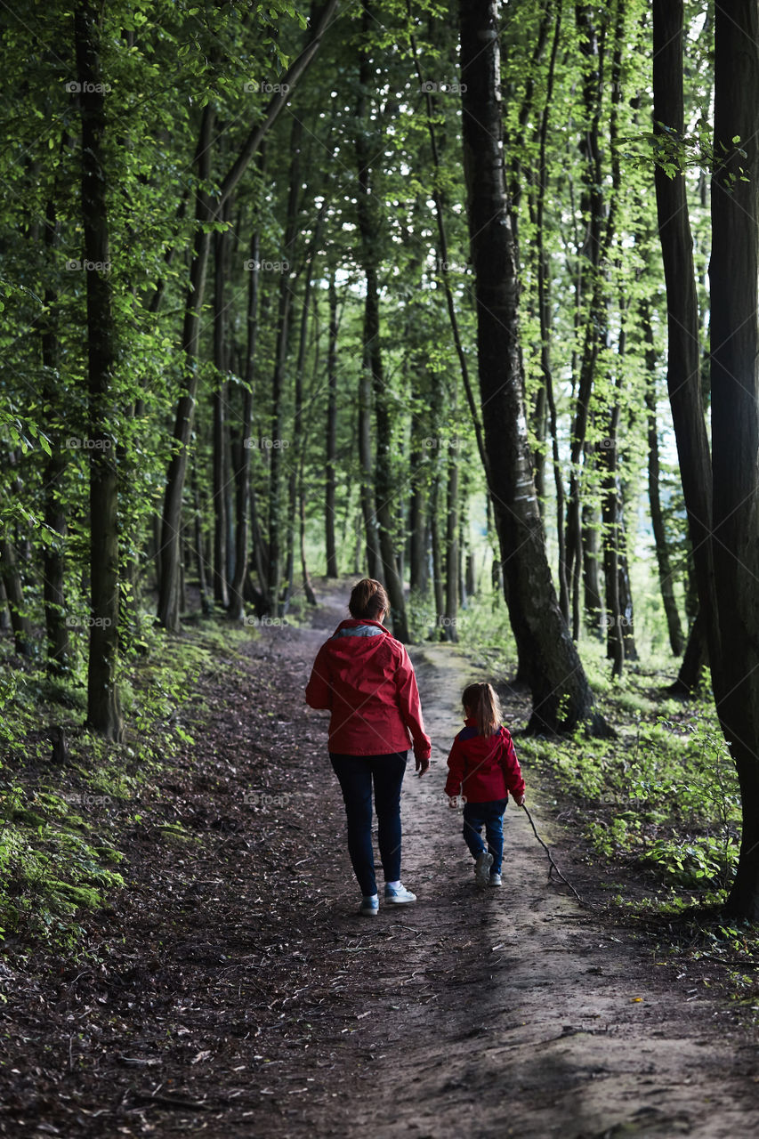 Mother with her little daughter walking through the forest. Spending leisure time, vacation on wandering in forests, close to nature