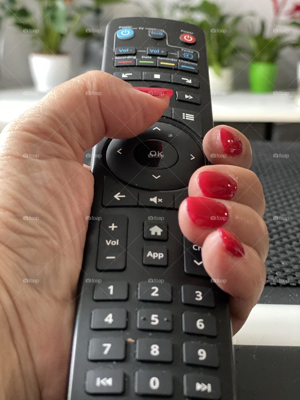 Hand with red manicure holding TV remote