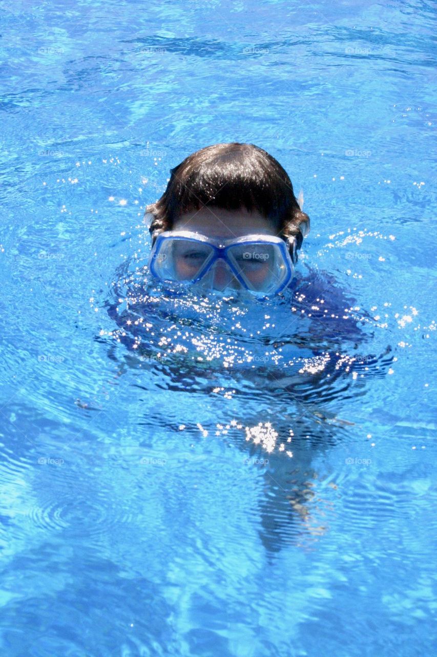 Kid with diving mask peeking from swimming pool water