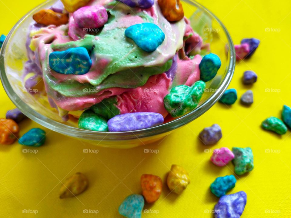 colorful ice cream mixture in the dish with colored chocolate pieces on yellow background