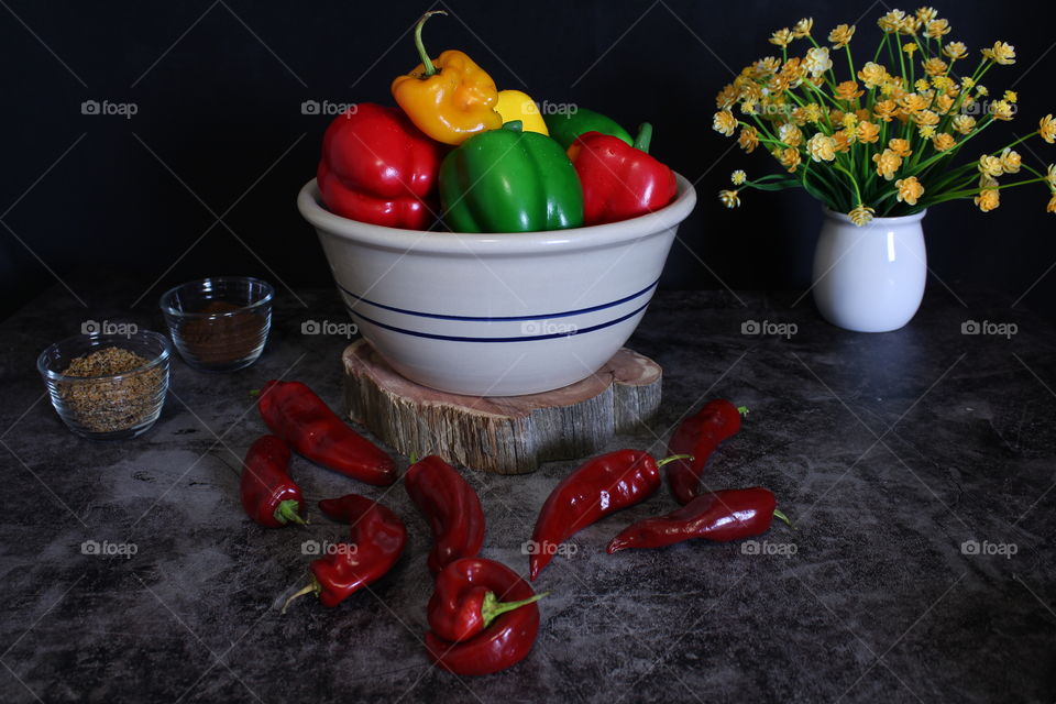 Large Bowl of Bell Peppers surrounded by Red Hot Peppers and Flowers