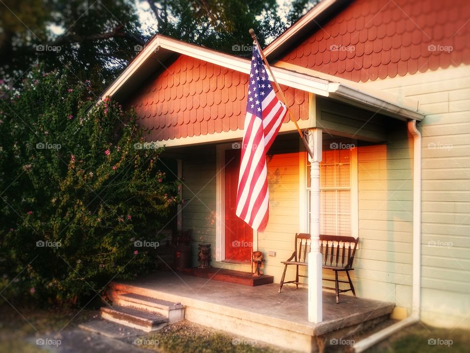 An American flag hanging on the front porch of a farm house