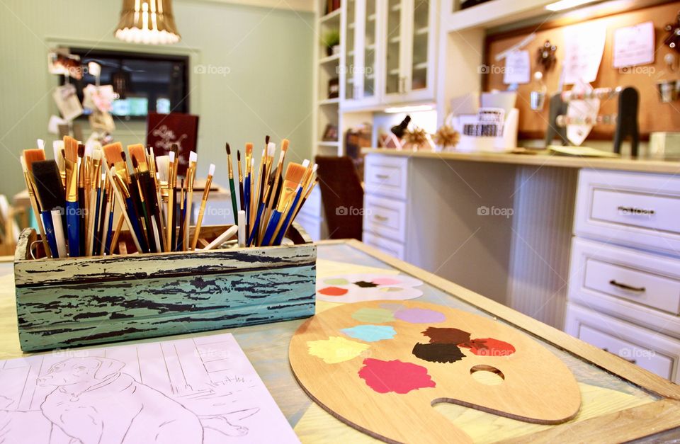 Distressed wooden basket with paint brushes and paint palette on a table in an art room.