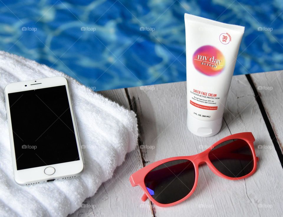 Poolside with towel, sunglasses, sunscreen  cellphone 