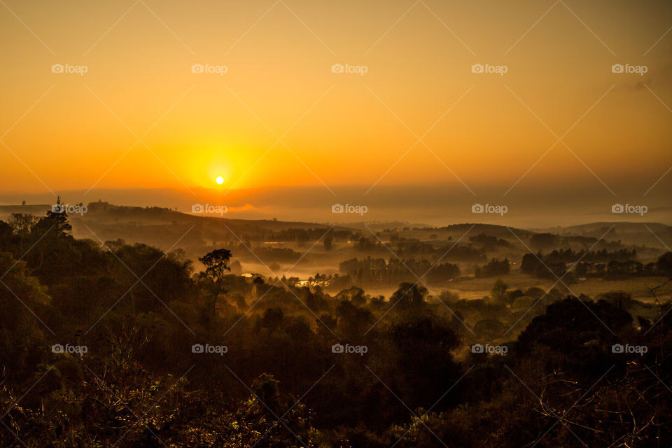 Sunrise over the valley with mist and trees on a cold winter's morning. Beautiful orange light through the clouds as the sun peeks through the fog.