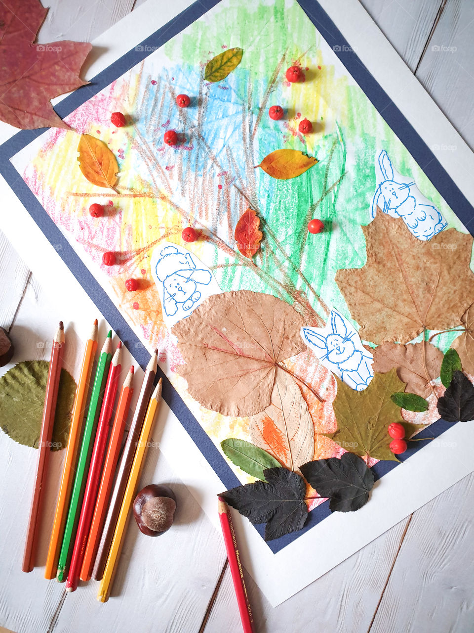 Children's creativity. Crafts, children's painting, application with autumn leaves and mountain ash on a light wooden background with chestnuts, multi-colored dry leaves and pencils