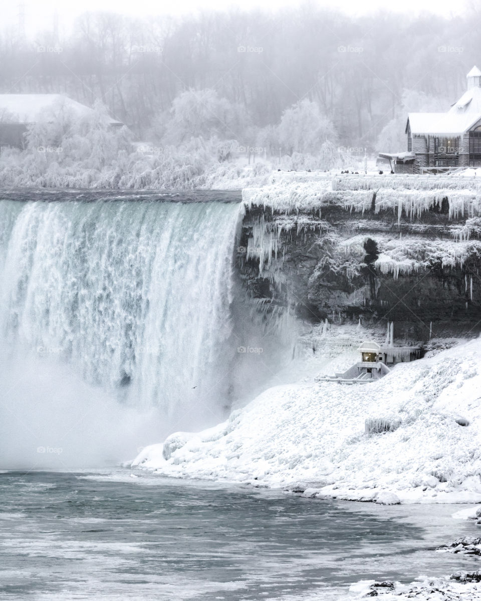 Frozen winter wonderland scene woth a massive waterfall next to a small structure