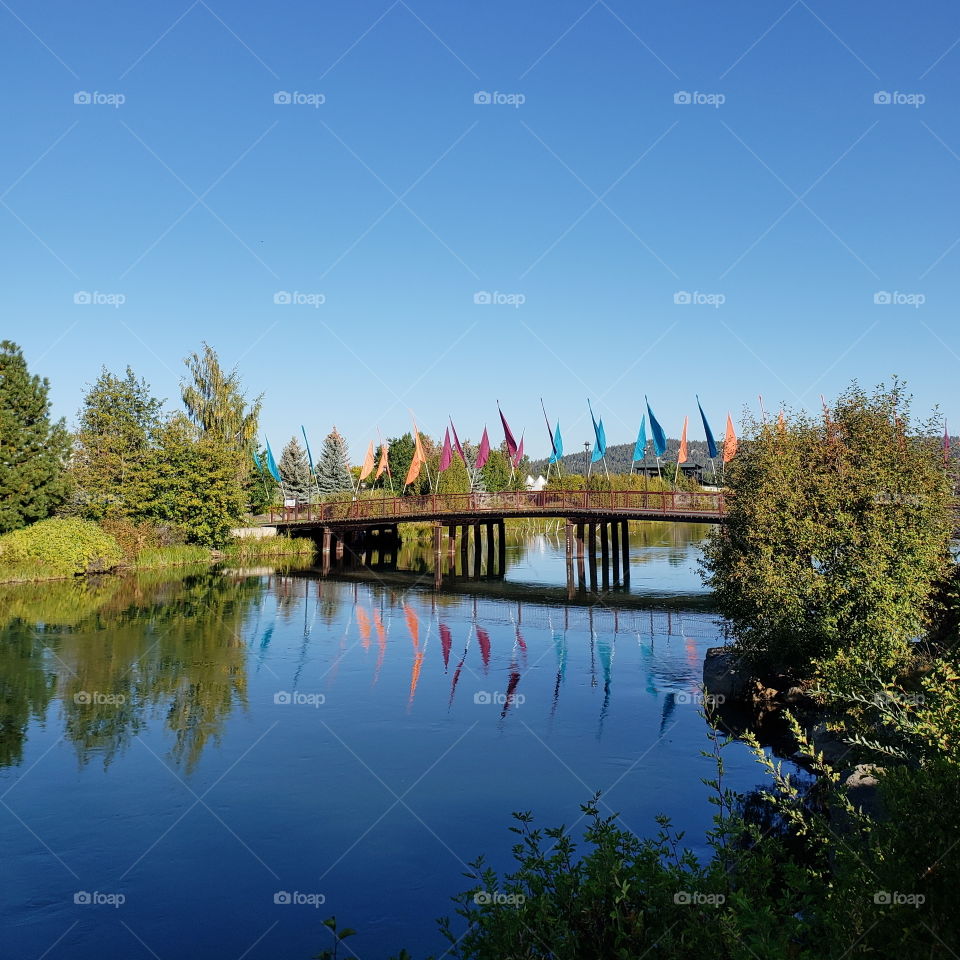 The wooden walking and biking bridge decorated with blue, orange, and pink flags in Bend’s Old Mill District on a beautiful fall morning in Central Oregon. 