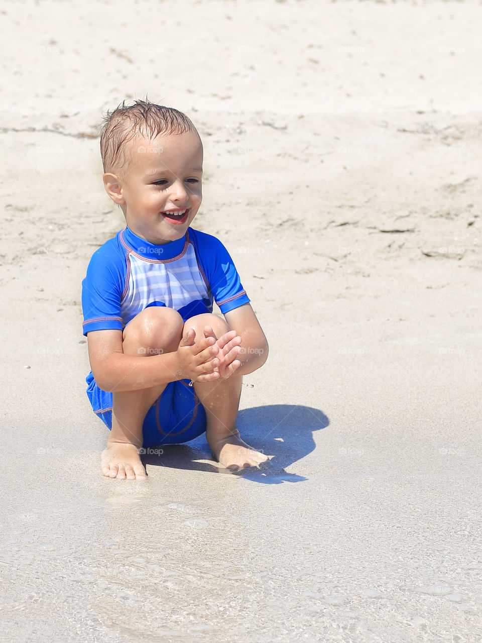 Little smiling boy is sitting on the beach