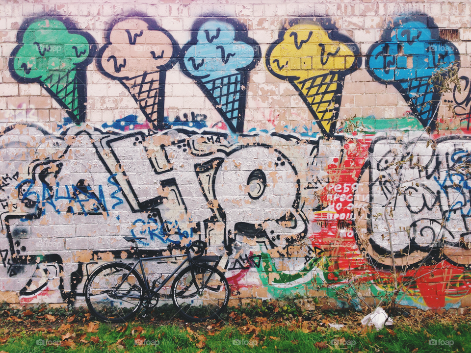 Grayish-black brakeless fixie bicycle standing in front of the wall decorated with bright colored wallart graffiti with ice-cream