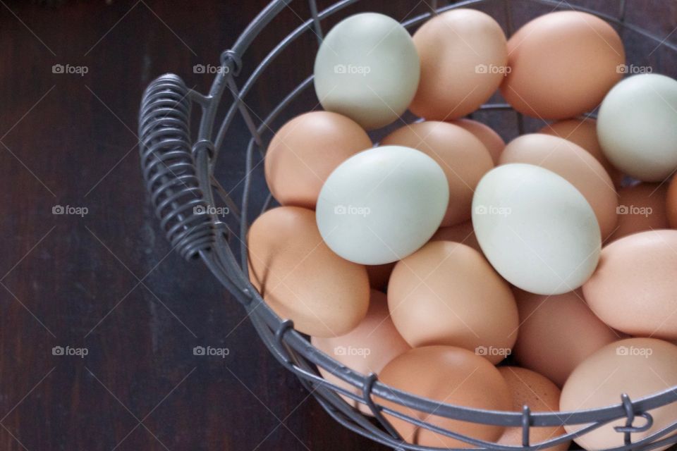 Farm-fresh blue and brown eggs in a wire basket on a dark wooden surface