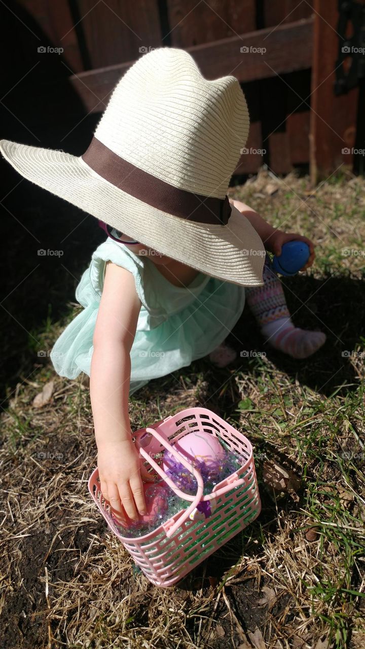 toddler finding Easter eggs dressed fancy in a sunhat and sunglasses