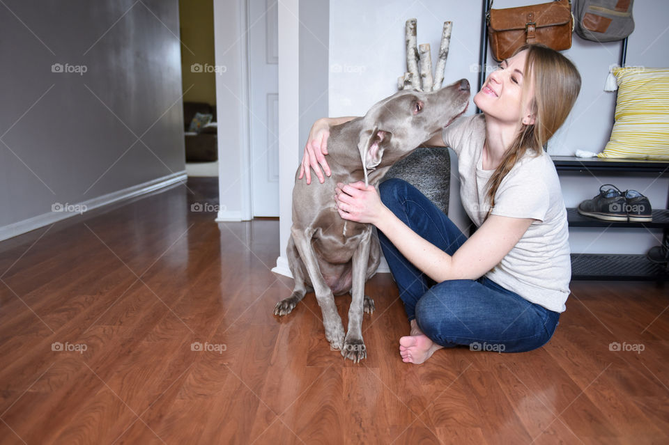 Millennial woman playing with her dog on a hardwood floor
