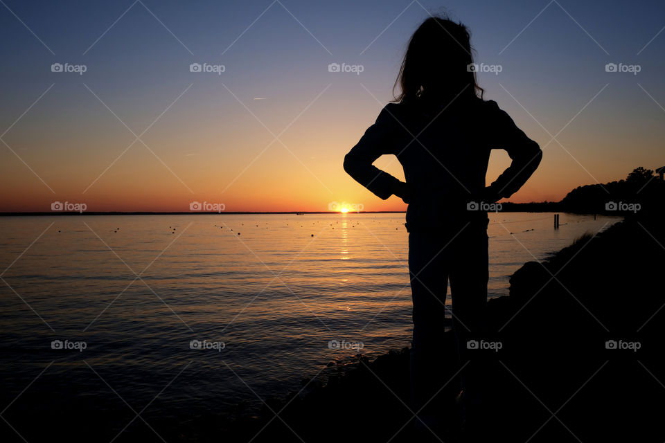 Little girl standing tall silhouetted by the golden sunset at the mouth or estuary of the Neuse River in Arapahoe North Carolina. 