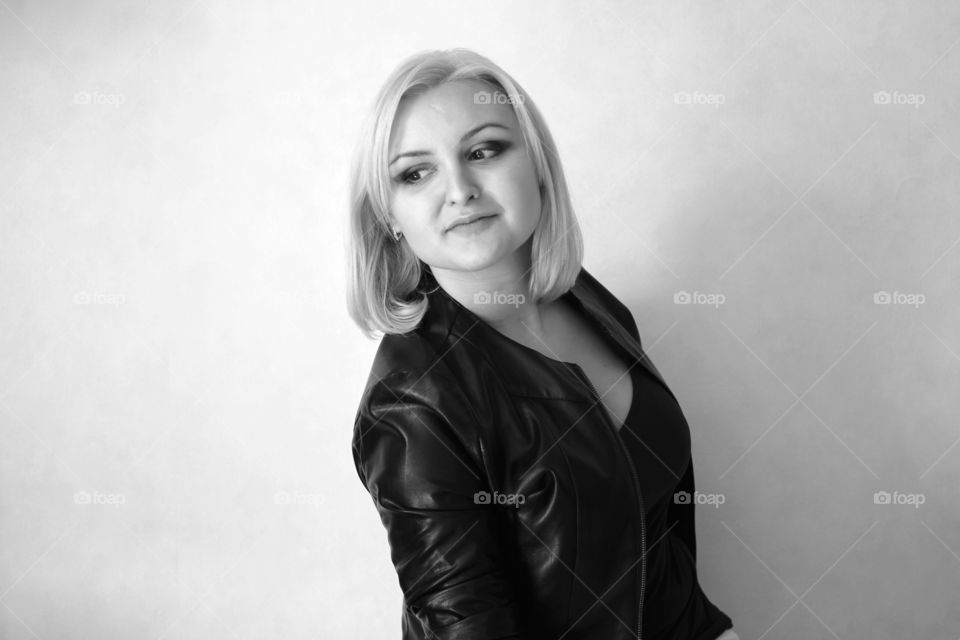 A blonde girl on a white background in a black leather jacket expresses her emotions and feelings (joy, sadness, amorousness, femininity, sensuality, tenderness)