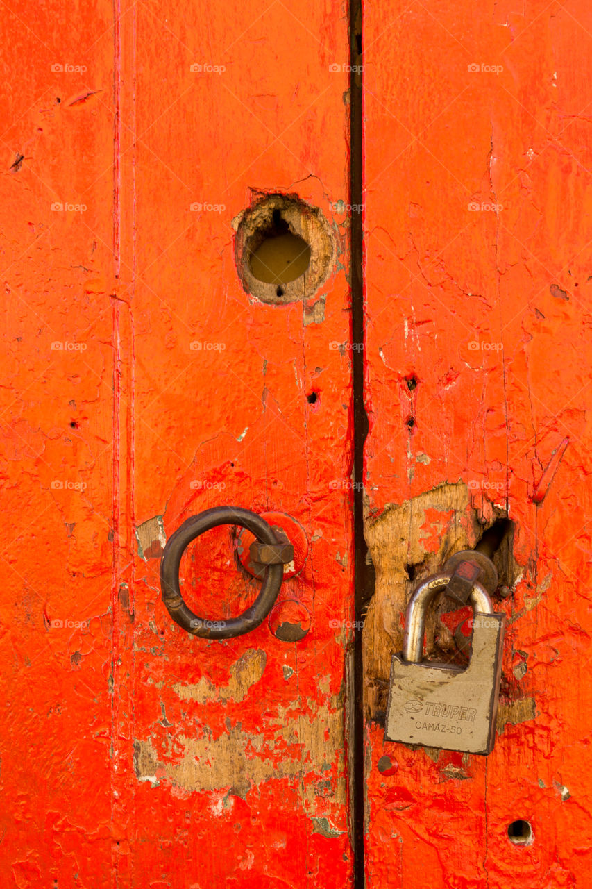 Worn red wooden door with lock. Aged wooden door with bright red paint, dark copper ring, golden lock and hole