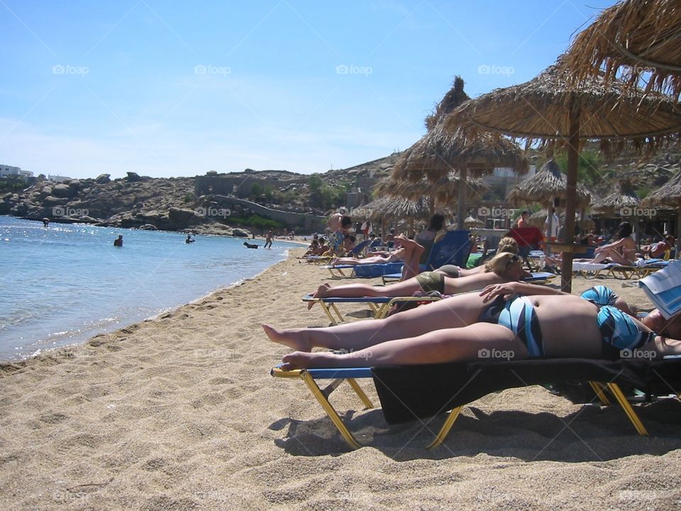 People basking in the summer heat on Paradise Beach in Mykonos, Greece.